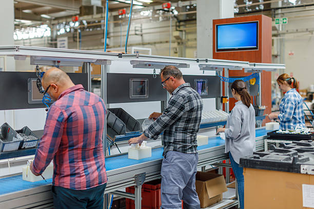 Concentrated professional young industrial factory workers team working with machine parts hands using electric pneumatic screwdriver retractable mechanism, fastened with screws in large Electric electronics wire and cable manufacturing plant factory warehouse