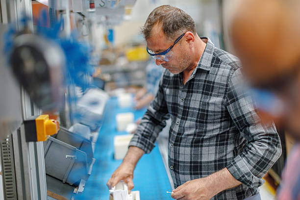 Concentrated professional young industrial factory workers team working with machine parts hands using electric pneumatic screwdriver retractable mechanism, fastened with screws in large Electric electronics wire and cable manufacturing plant factory warehouse