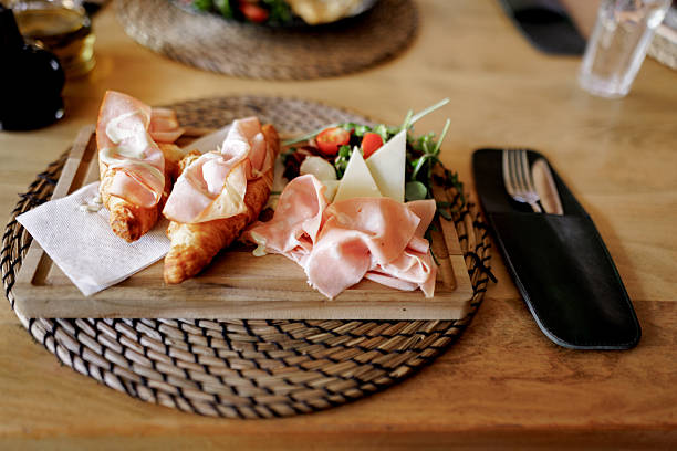 A freshly baked croissant filled with ham is served on a plate at a restaurant, presented as a delicious and appetizing breakfast or brunch option.