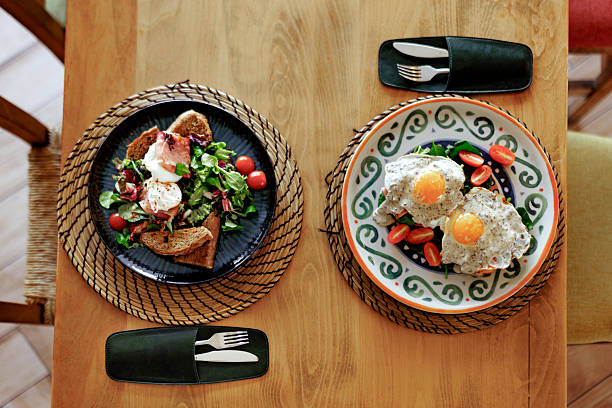 A top-down view of a breakfast spread at a restaurant, featuring a plate of fried eggs with tomatoes and spinach, alongside poached eggs on toasted bread with spinach and tomatoes, beautifully arranged for a colorful and appetizing presentation.