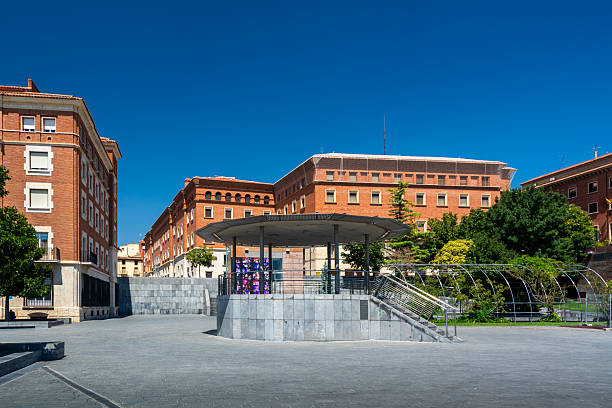 Teruel, Spain - August 15, 2022: View of Plaza de la Glorieta with modern structures, red brick buildings, and greenery under a clear blue sky.