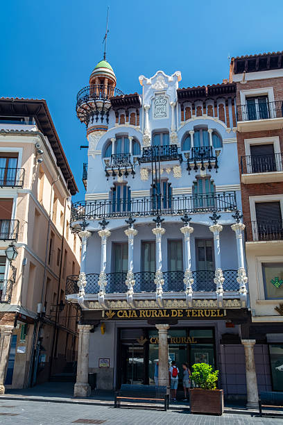 Teruel, Spain - August 15, 2022: View of the modernist Casa Ferran built in 1912, now housing Caja Rural de Teruel bank, with pedestrians on the sidewalk.