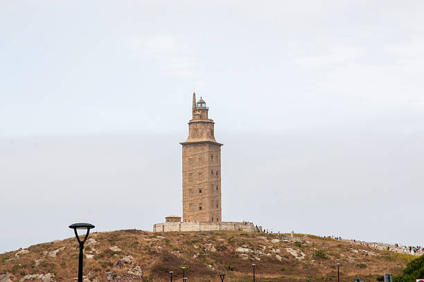 Tourists gather around the historic tower in La Coruna, Spain on a sunny day.