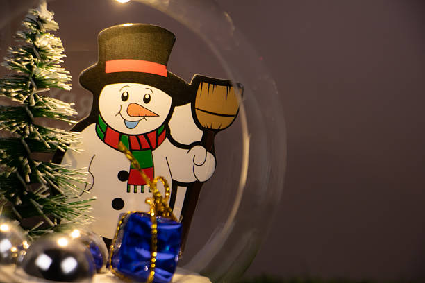 Cute snowman decoration inside a glass dome with Christmas tree and gift, warm light and copy space, festive winter holiday concept.
