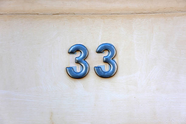 istock Metallic number 33 mounted on a beige wall of a building 2257488783