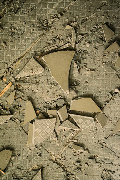 Broken tiles scatter amongst cracked concrete rubble, creating an abstract pattern of destruction. Stark lighting highlights the gritty textures and industrial damage, conveying a desolate mood.