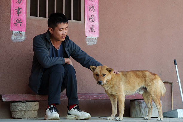 The Asian man is petting his mixed-breed dog.