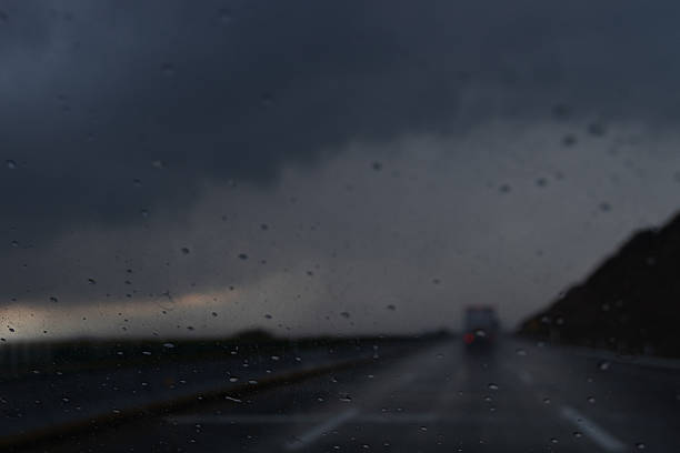 View of a highway during rainy weather at dusk, seen through a vehicle windshield with raindrops and low visibility.