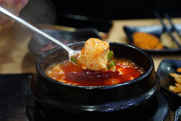 Asian woman holding a piece of kimchi and tteokbokki while enjoying Korean kimchi soup