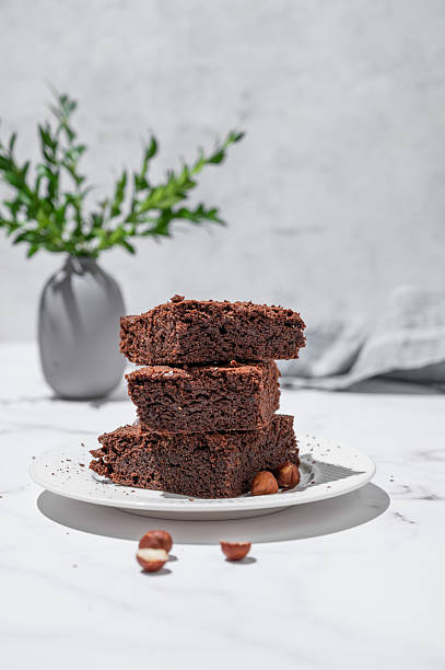 Chocolate brownie on a plate on a marble background with nuts branch and morning shadow.