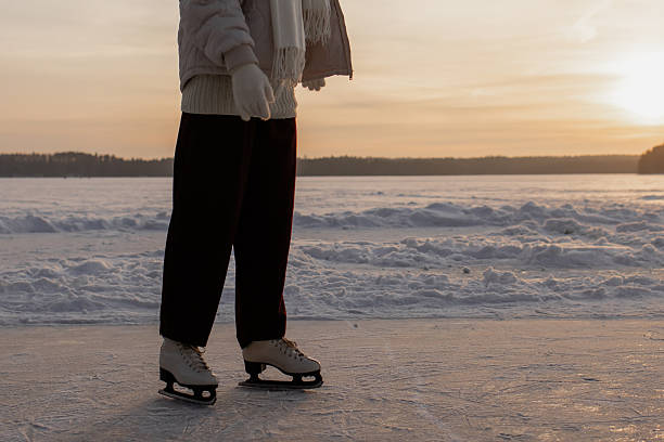 LENS FLARE, CLOSE UP: White ice skates glide across glossy natural ice during warm winter evening light. Golden reflections and a calm winter mood while ice skating on frozen Lake Cerknica, Slovenia.