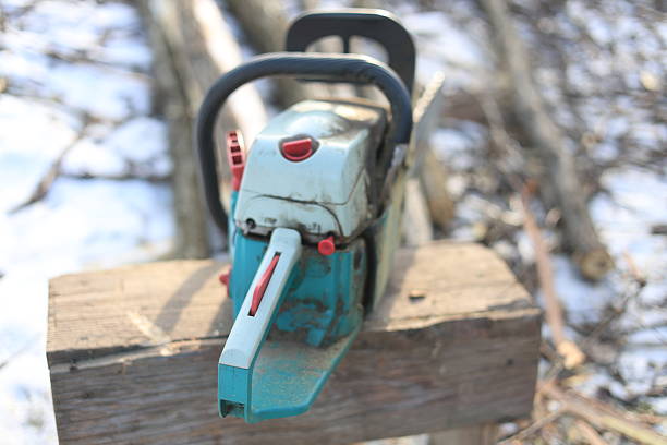 A chainsaw is resting on a hardwood flooring. The machine is powered by gas and is commonly used in automotive tire and wheel systems. It has metal parts