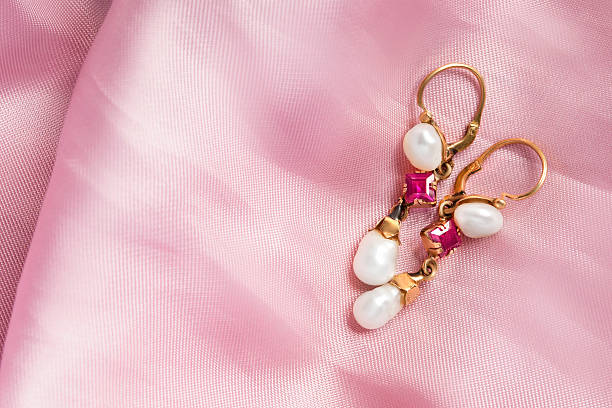 Vintage pearl golden earrings lying on pastel pink satin background
