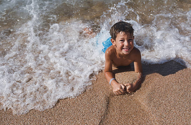 Smiling boy lying on sandy beach with waves splashing around
