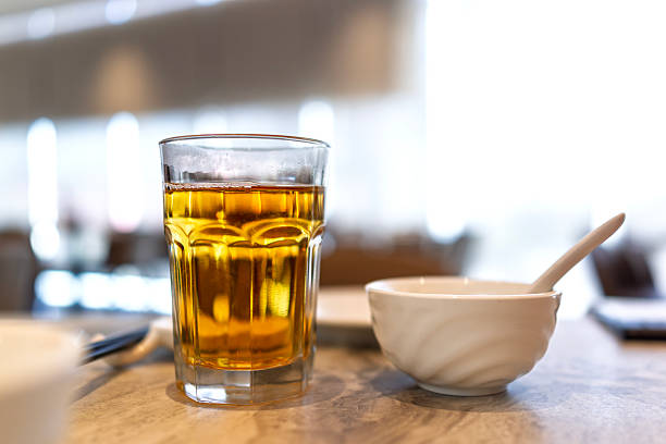 Close-up view of Chinese tea served in a clear glass placed on a restaurant table, accompanied by a small ceramic bowl and spoon.
