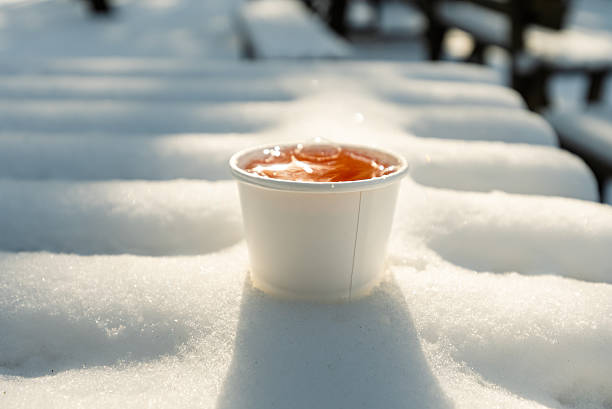A cup of coffee is poured into a paper cup on a snowy surface. The cup is empty and the snow is covering the ground. The scene is peaceful and serene