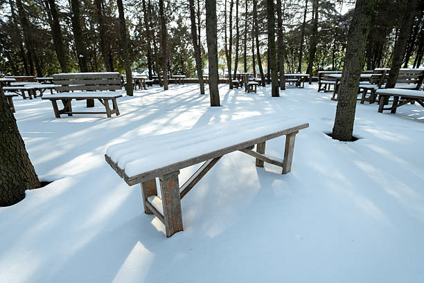 A bench covered in snow sits in a park. The bench is surrounded by snow and is the only one in the area