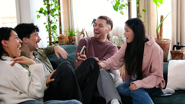 Diverse friends enjoying humorous content on a smartphone, laughing together on a sofa at home