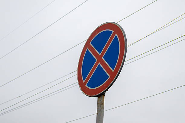 A vibrant no parking sign captures attention under a grey sky, surrounded by power lines and hinting at urban regulations in effect.