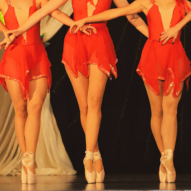 Three ballet dancers perform on pointe on a theater stage, wearing matching red costumes and classical ballet shoes. The composition focuses on synchronized movement, balance, and elegant posture, highlighting teamwork and precision in a live dance performance. The image represents performing arts, discipline, and artistic expression.