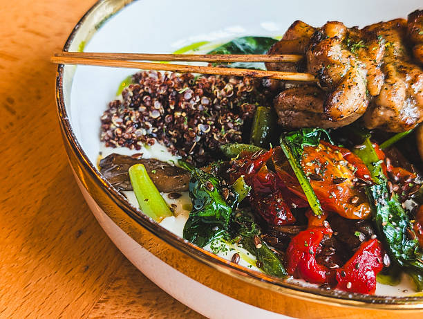 Side view of grilled chicken skewers with quinoa and roasted vegetables in a bowl