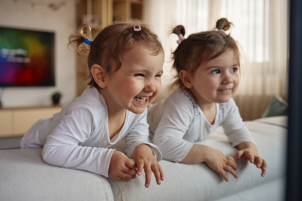 Two sweet little girls stand in their preschool room as they hug and smile for a portrait.  They are both dressed casually and appear happy.