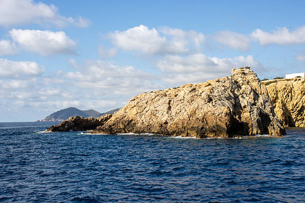 typical rock headland with cliff and trees with a cloudy sky in Ibiza, Spain