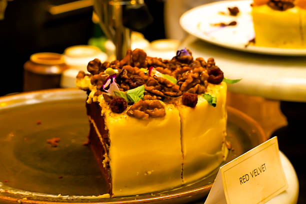 A rich red velvet cake slice with creamy white frosting, generously topped with crunchy walnuts and small berries.