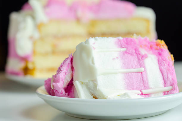 A slice of cake with pink frosting on a white plate. The cake is cut into layers and has a pink frosting on top