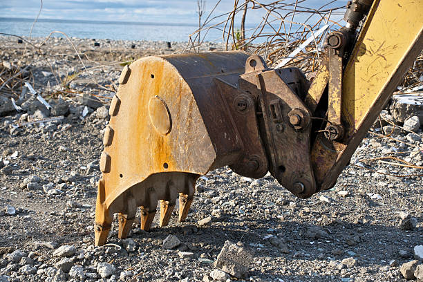 Rusty Excavator Bucket and Rebar on Construction Demolition Site. Close-up of Old Rusty Excavator Bucket with Exposed Rebar Against Blue Sky