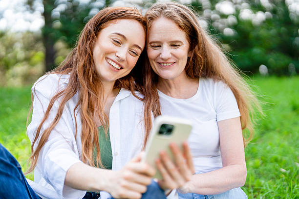 istock Two women share a moment while looking at a mobile phone in a green park during daytime 2257563106