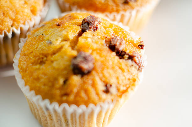 A close up of a muffin with chocolate chips on top. The muffin is sitting on a white plate