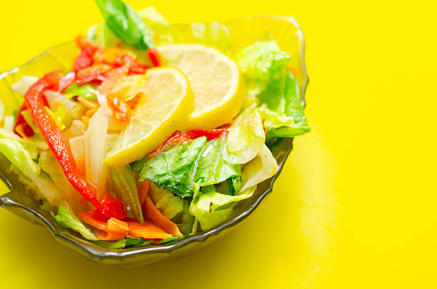 A bowl of salad with a lemon slice on top. The salad is a mix of vegetables including carrots and peppers
