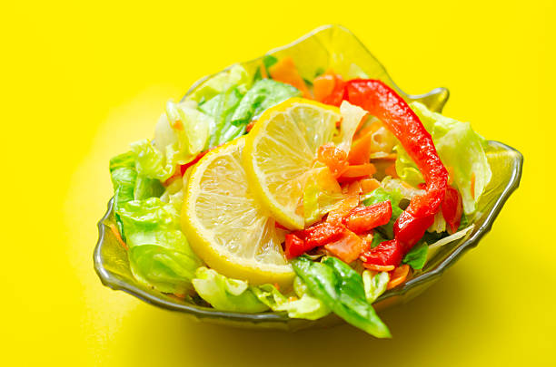 A bowl of salad with a lemon slice on top. The salad is a mix of vegetables including carrots and peppers