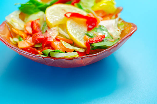 A bowl of salad with a lemon slice on top. The salad is a mix of vegetables including carrots and peppers