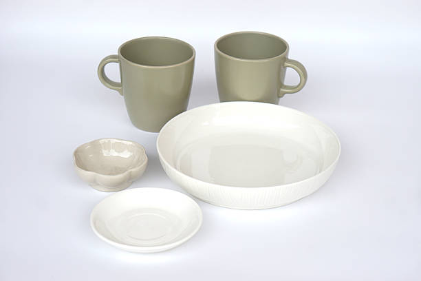 Minimal ceramic tableware set including two matte green mugs, white bowl, small plate and textured dipping bowl isolated on white background. Modern kitchenware concept for dining, home decor and lifestyle use.
