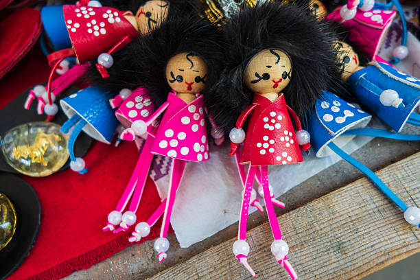 many small dolls with painted faces and colorful outfits are arranged on wooden table at local market. vendors showcase traditional crafts to visitors. close up.
