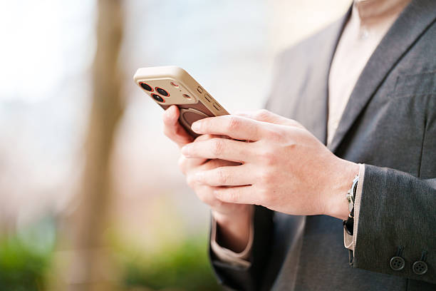 Close-up view of an adult man’s hands using a smartphone outdoors in a modern urban environment. Cropped composition highlights mobile technology, digital communication, and everyday modern lifestyle in a public space.
