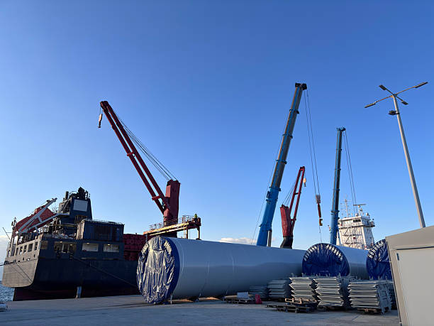 Wind turbine towers waiting to be transported at a port with a crane
