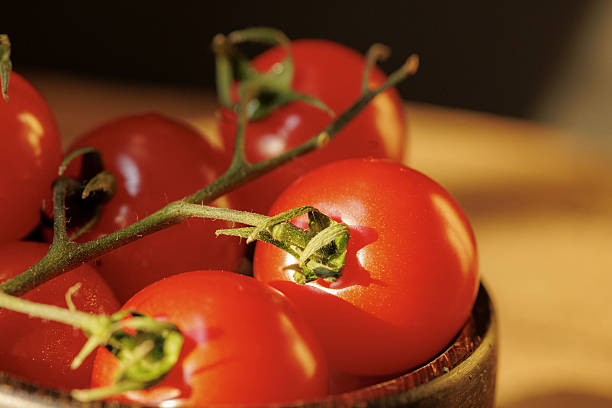 Fresh red tomatoes on vine in wooden bowl, illuminated by warm sunlight, creating vibrant and appetizing scene. tomatoes glossy skin and rich color highlight their ripeness
