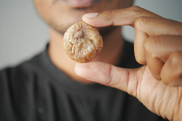 Person displays a dried fig with an expression of curiosity and satisfaction.