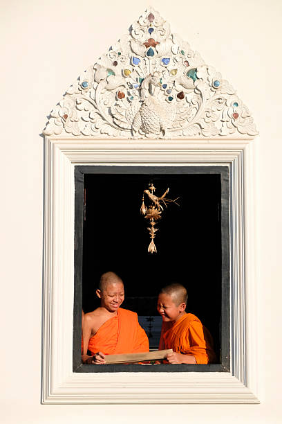 Buddhist novice wearing a robe reads a book by a window with soft morning light