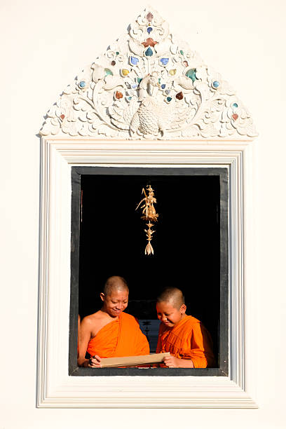 Buddhist novice wearing a robe reads a book by a window with soft morning light