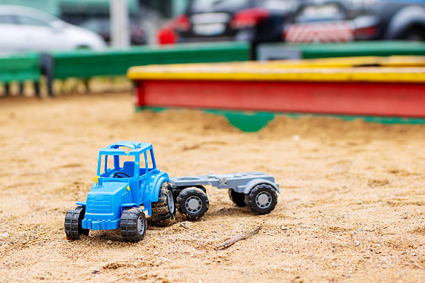 A vibrant blue toy tractor, complete with a small trailer, is currently sitting amidst the soft sand in a sandbox