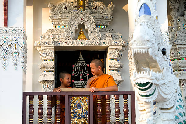 Buddhist novice wearing a robe reads a book by a window with soft morning light
