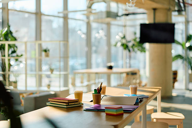 Modern coworking office space featuring a long wooden desk with notebooks, pens, and coffee cups, creating a bright and productive environment for work, study, and collaboration