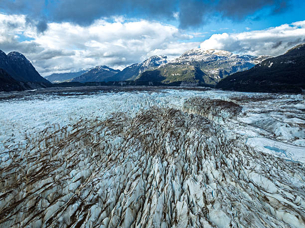 Detailed view of deep crevasses and textured ice patterns leading toward distant snow-capped mountains. The composition highlights natural lines, scale, and the rugged beauty of glacial landscapes in Chilean Patagonia.