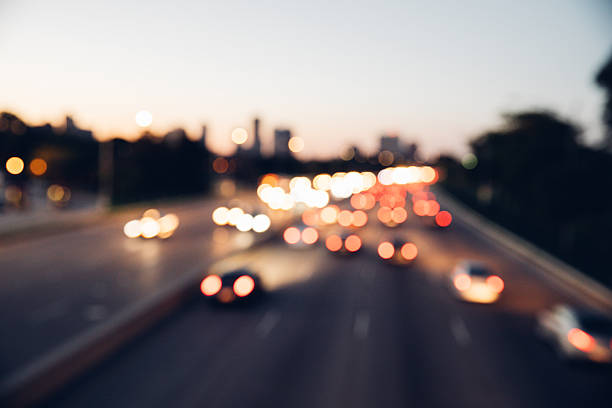 Cars driving along a multi-lane urban highway during early evening. Motion blur suggests movement and daily commuting. Image represents transportation, rush hour, and city mobility.