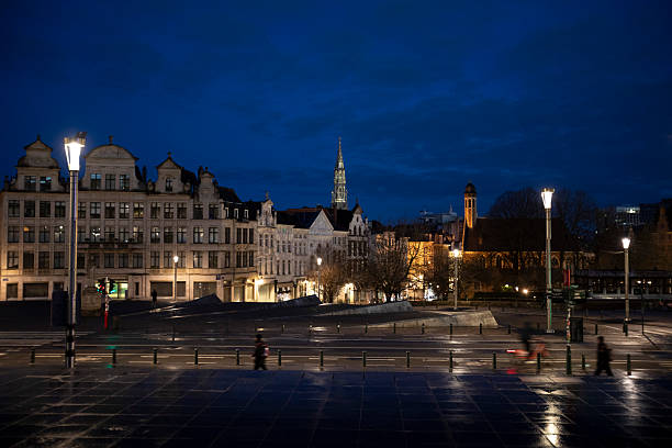 Brussels city skyline viewed from Mont des Arts just before sunrise. The tower of Brussels Town Hall can be seen on the horizon, and people on the move are in the foreground.