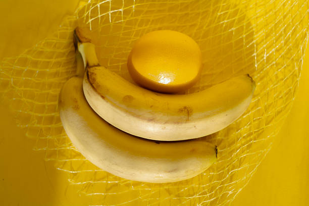 Close-up of a fresh yellow lemon delicately wrapped in translucent yellow mesh netting, placed on a vibrant monochromatic yellow background. Conceptual still life image evoking themes of freshness, protection, packaging, fragility, citrus fruit, and summer vibes. Minimalist abstract composition with rich texture details, soft lighting, and high visual impact.